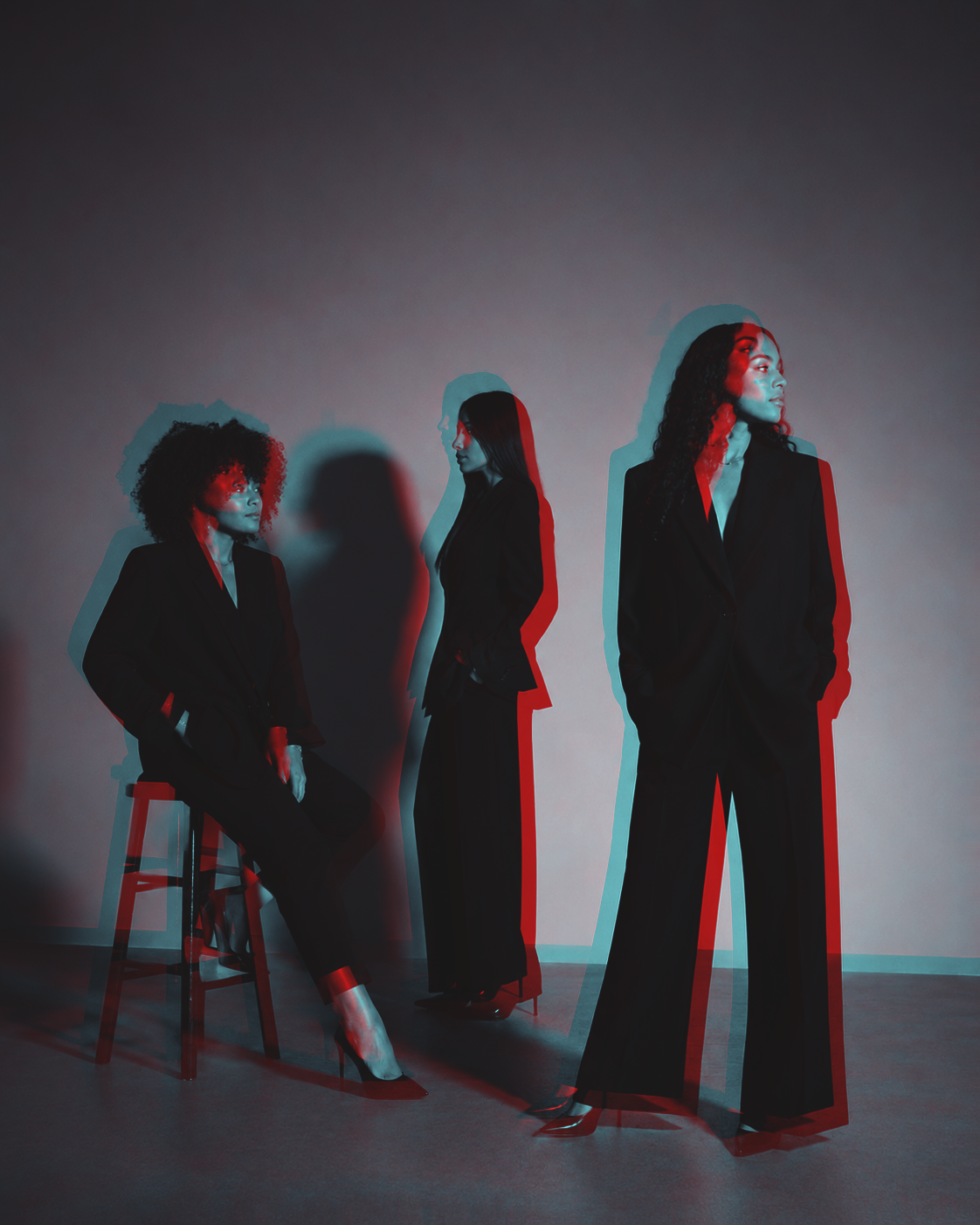 Tres profesionales en trajes negros en una composición editorial con luz roja y azul
